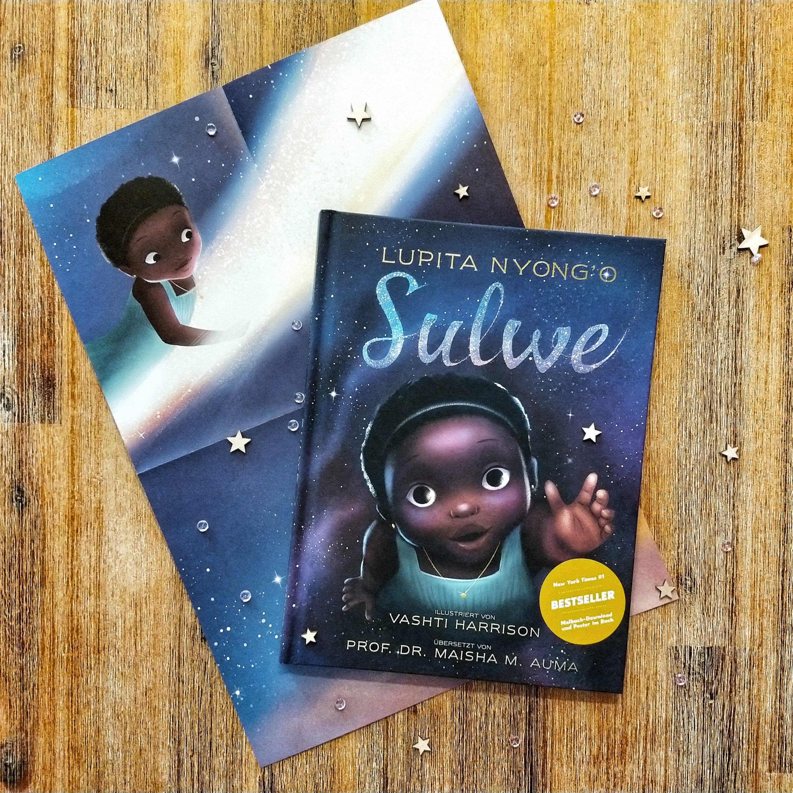 Auf einem Holzhintergrund liegt das Buch "Sulwe". Auf dem Cover ist die Illustration eines Schwarzen Mädchens zu sehen, das mit der Hand nach oben greift. Das Buch liegt auf einem halb zusammengefalteten Plakat, das Sulwe zeigt, die auf der Sternschnuppe reitet.
